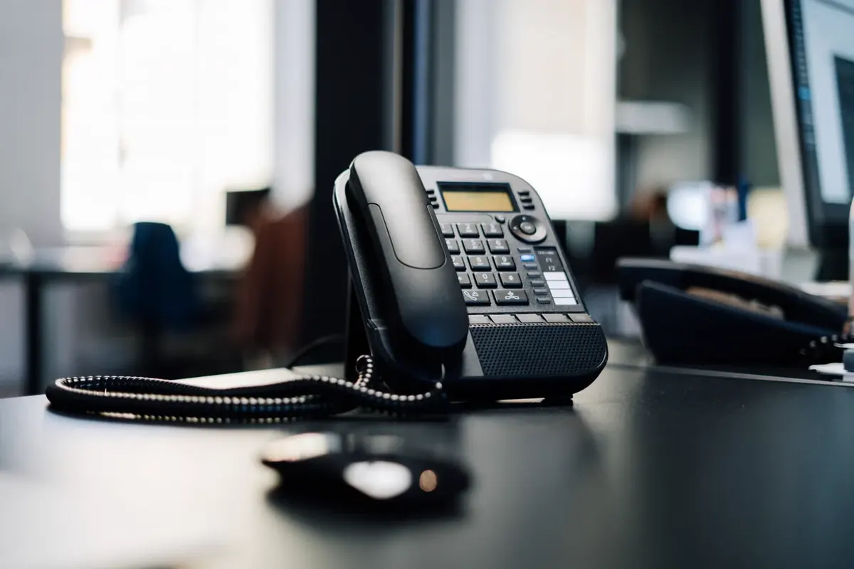 Close-up of a black desk VoIP handset on an office desk with the workspace blurred behind it