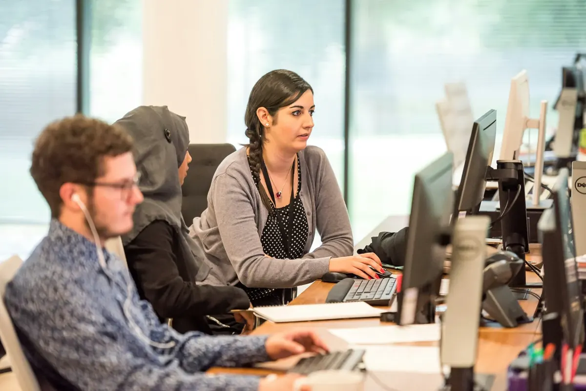A small office team working side by side at desks with multiple monitors, a desk phone and earphones in use