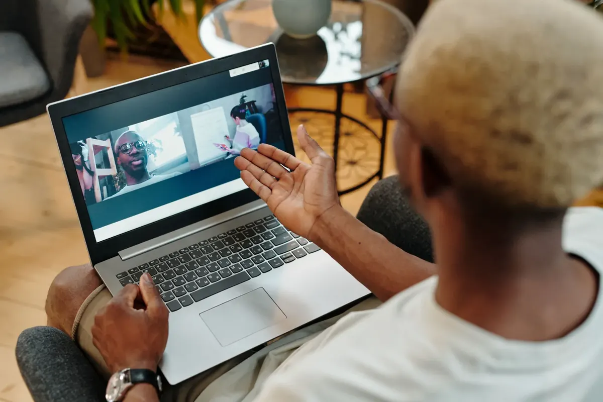 A man on a laptop video call with colleagues, seen over his shoulder while working from home
